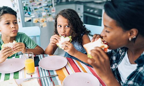 Woman and two kids sitting at a table eating.